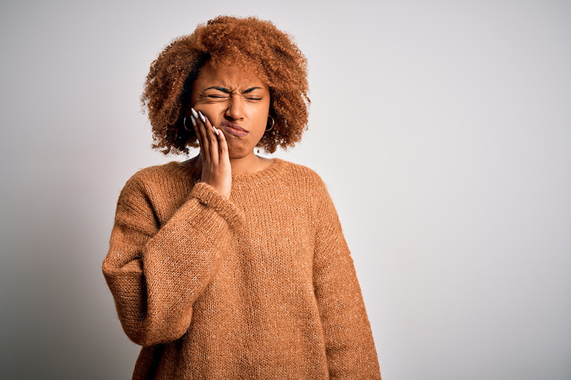 Mulher com mão na bochecha porque está sentindo dor na gengiva