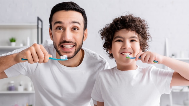 Pai e filho em escovando os dentes com Colgate Total para ter 24 horas de proteção