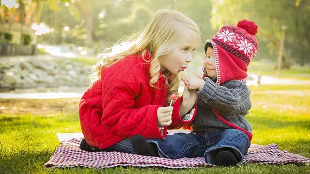 Bebê dividindo um pirulito com uma menina no parque