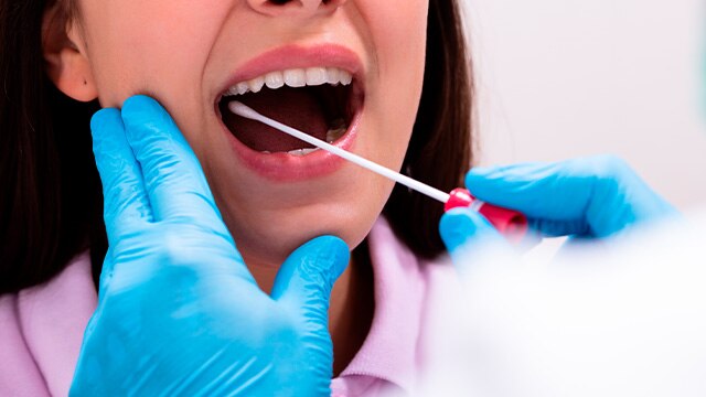 menina de boca aberta sendo examinada pelo dentista com um cotonete