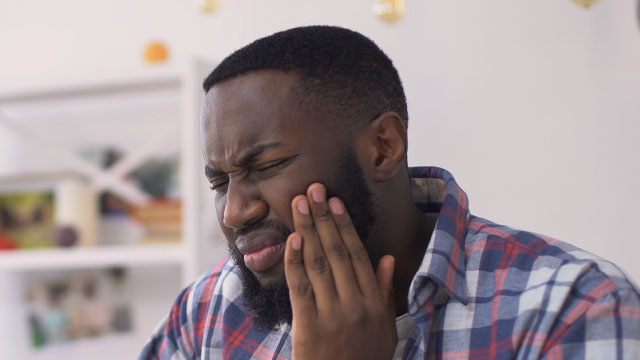 Homem sentindo dente dolorido ao morder com a mão no rosto