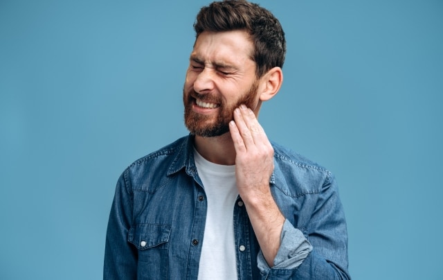 Foco em uma mulher com a boca entreaberta, levando a mão à bochecha para representar a dor causada pela infecção no dente.