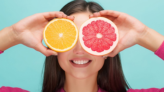 Mulher sorridente segurando fatias de frutas exóticas, como a toranja, cobrindo os olhos