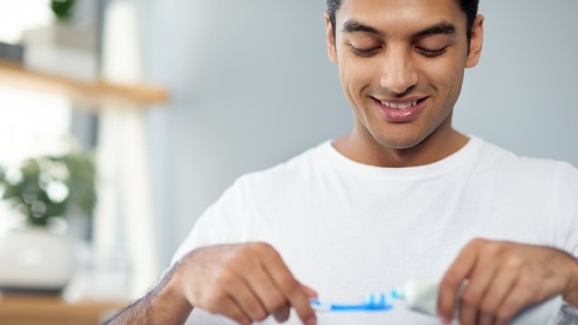 Homem sorrindo enquanto coloca a melhor pasta de dente na escova para escovar os dentes