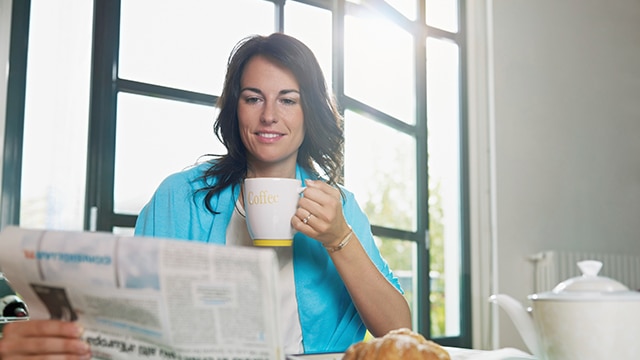 mulher sorrindo lendo o jornal durante o café da manhã.