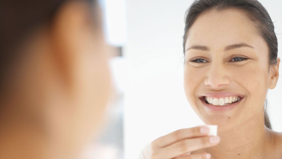mulher com cabelos longos escuros amarrados, sorrindo e segurando um recipiente para bochecho com óleo.