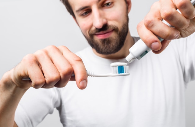 Homem colocando uma opção de pasta de dente barata na sua escova para escovar os dentes