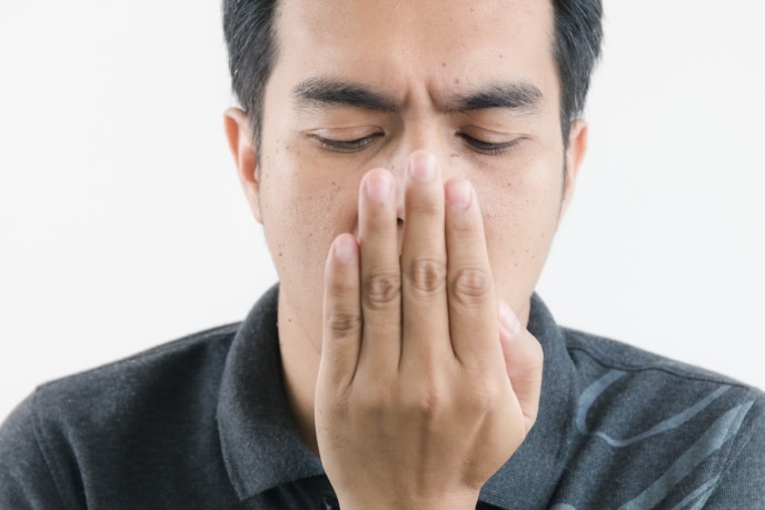 Homem verificando se está com bafo e precisa comprar uma pasta de dente para mau hálito