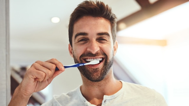 Homem sorrindo e escovando os dentes com sua escova de dente macia