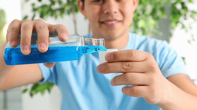 Homem sorridente despejando enxaguante bucal com flúor no copo dosador, pronto para o uso.