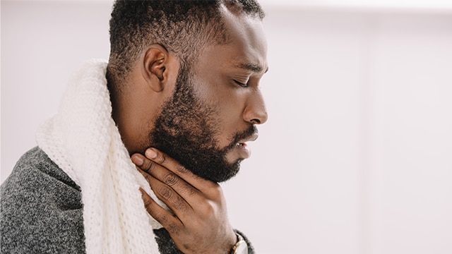 Homem com expressão de dor na garganta, usando cachecol e tocando o pescoço com a mão, preocupado com a possibilidade de ser síndrome de Eagle.