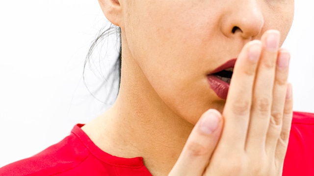 Mulher de blusa vermelha cobrindo a boca com a mão, sugerindo preocupação com mau hálito constante.