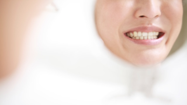 sorriso de mulher em tom amarelado refletido em espelho redondo de banheiro.